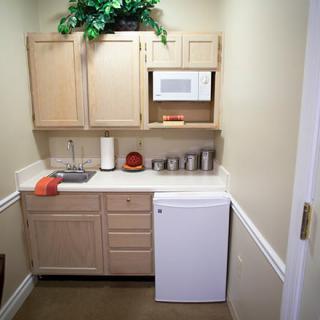 A compact kitchenette with wooden cabinets, a microwave, and a small refrigerator.