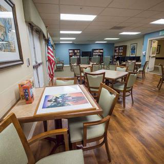 A well-lit room with several tables and chairs, featuring wooden flooring and an American flag in the corner.
