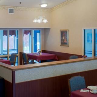 An empty restaurant dining area with tables and chairs arranged neatly, featuring large windows for natural lighting.