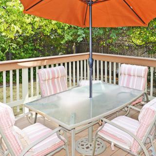 A patio setup with a glass table, cushioned chairs, and an orange umbrella on a wooden deck.