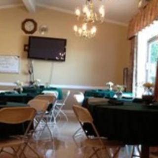 A well-lit room with multiple tables and chairs, featuring a wall-mounted television and a chandelier.