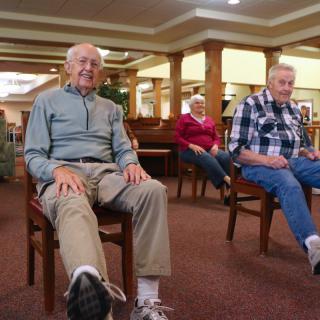 A group of elderly individuals participating in a seated exercise session indoors.