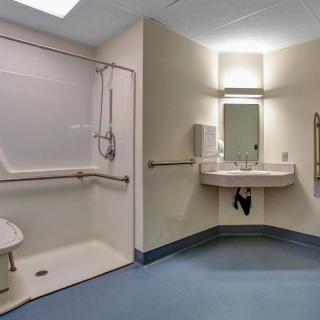 An accessible bathroom featuring a wheelchair-friendly shower with a built-in seat and grab bars, alongside a sink with a mirror.