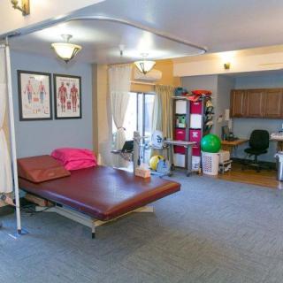 A physical therapy clinic room equipped with a treatment table, exercise equipment, and anatomical charts.
