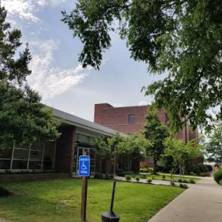 A view of a modern building surrounded by green trees and well-maintained grass, featuring an accessible parking sign.