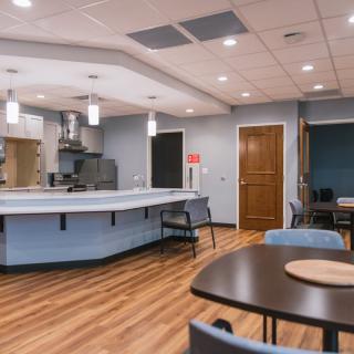 A modern kitchen and dining area with wood flooring, featuring a central island, pendant lighting, and several tables and chairs.