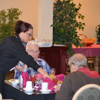 A waitress serving drinks to elderly patrons at a restaurant.