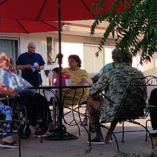 A group of elderly individuals enjoying a pleasant afternoon conversation under red umbrellas.