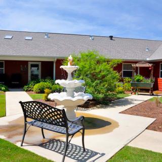 A serene courtyard featuring a fountain, surrounded by greenery and a bench for relaxation.