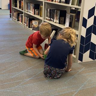 Two children sitting on the floor, exploring books in a library.