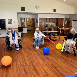 Elderly residents engage in a playful activity using colorful balls in a rehabilitation setting.