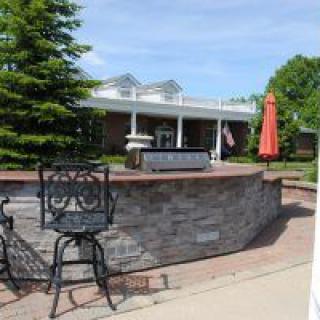 An outdoor patio area with bar stools, a stone counter, and an umbrella, located next to a building.