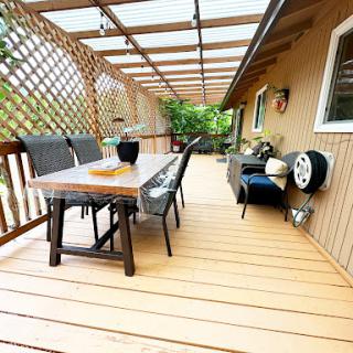 A cozy outdoor deck featuring a wooden table, comfortable seating, and beautiful greenery.