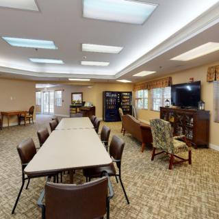 A spacious community room with tables and chairs arranged for meetings, featuring a TV and comfortable sofas.