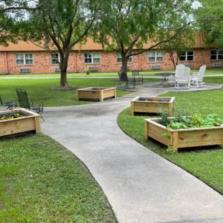 A well-maintained garden area featuring raised planter beds and a winding pathway surrounded by trees.