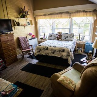 A cozy bedroom with a neatly made bed, television, and large windows letting in natural light.