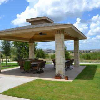 An outdoor gazebo with seating, set in a landscaped garden.