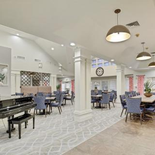 A spacious and elegantly decorated dining area featuring neatly arranged tables and chairs, a grand piano, and stylish chandeliers.