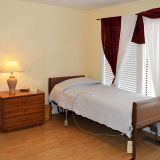 A simple bedroom with a single bed, wooden dresser, and a lamp beside a window with curtains.