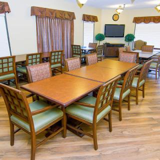 A well-arranged dining room with wooden tables and chairs, featuring a television and decorative elements in the background.