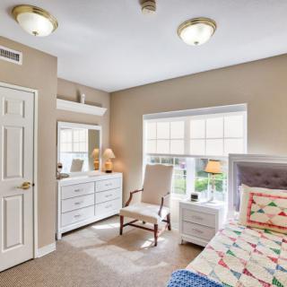 A cozy bedroom featuring a bed with colorful bedding, a white dresser, and a comfortable chair by the window.