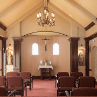 A serene chapel interior with an altar, wooden chairs, and a chandelier.