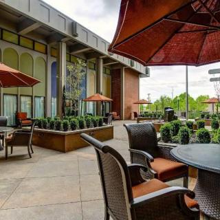 A cozy outdoor patio with tables, chairs, and umbrellas, surrounded by lush greenery.