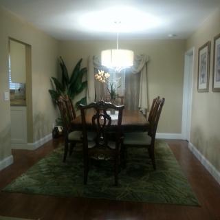 A well-lit dining room featuring a wooden table set, surrounded by chairs, adorned with a chandelier and indoor plants.