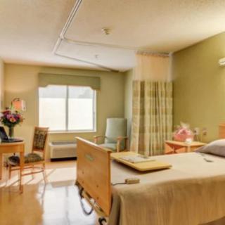 A well-lit hospital room with a patient bed, chairs, and medical equipment.