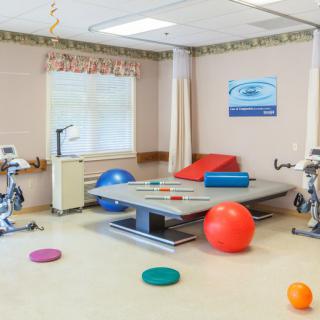 A well-equipped physical therapy room featuring exercise balls, a therapy table, and stationary bikes.