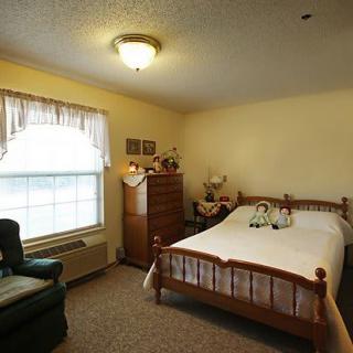 A cozy bedroom with a wooden bed, dresser, and a large window.