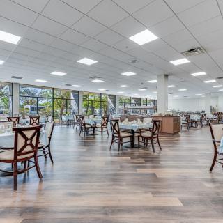 A modern dining area with wooden floors, empty tables and chairs, and large windows.