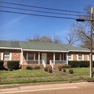 A single-story brick house with a front porch and manicured lawn.