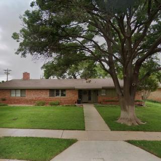 A single-story brick house with a large tree in the front yard and well-maintained lawn.
