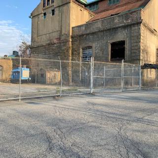 A fenced-off area in front of an old, abandoned warehouse with a clear sky in the background.