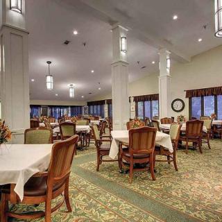 A spacious dining room with neatly arranged tables and chairs, adorned with elegant lighting and carpeted flooring.