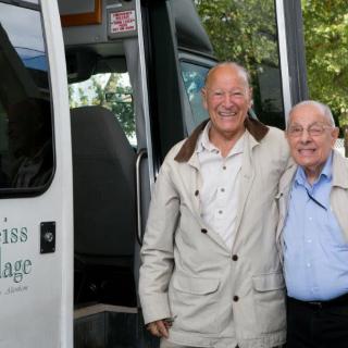 Two elderly men smiling and standing next to a bus outdoors.