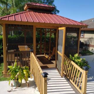 A cozy wooden gazebo with a red roof in a garden setting, surrounded by plants.