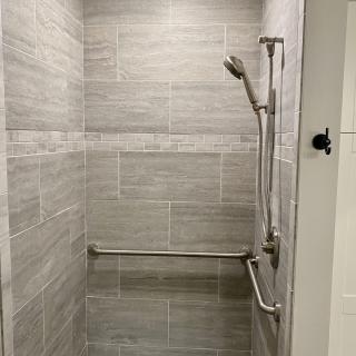 A tiled shower with a handheld showerhead and a grab bar.