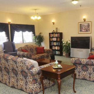 A cozy living room with patterned sofas, a wooden coffee table, and a television near a bookshelf beneath soft lighting.