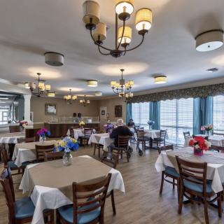 A well-lit dining area with neatly arranged tables and chairs, adorned with chandeliers and decorative table settings.