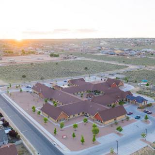 Aerial view of a building complex at sunset, surrounded by a residential area and open land.