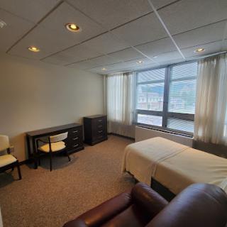 A spacious room featuring a bed, desk, and comfortable seating with large windows providing natural light.