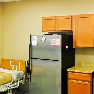 A small kitchen area with a refrigerator, wooden cabinets, and medical equipment nearby.