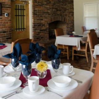 A cozy dining area with elegantly set tables featuring blue napkins and a single yellow flower centerpiece.