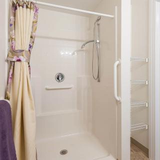 A clean and simple walk-in shower with a floral curtain and grab bar.