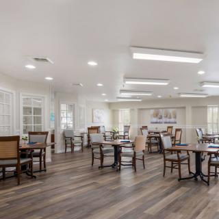 A spacious and modern dining room with multiple tables and chairs, illuminated by bright lighting.