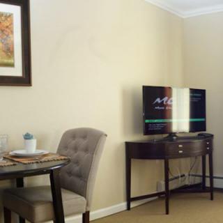 A cozy living room with a TV on a stand, a small round table with two chairs, and a framed picture on the wall.