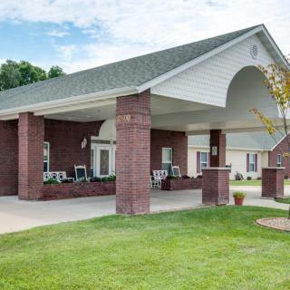 A building entrance with a covered area supported by brick columns, set in a landscaped outdoor environment.