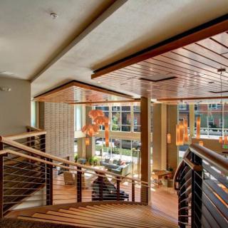 A modern interior featuring a wooden staircase, elegant chandeliers, and abundant natural light.